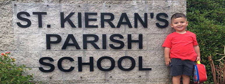Student stands next to an outdoor St. Kieran sign
