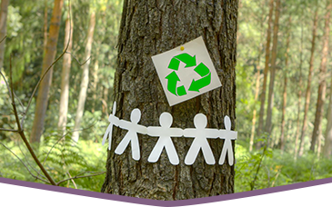 A tree in the forest with a recycling logo and paper craft people attached to it